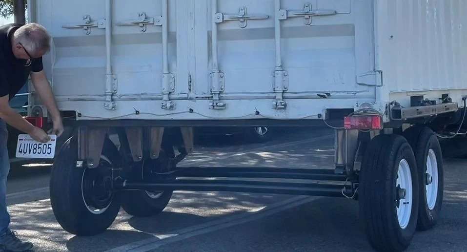 Man inspecting undercarriage of white semi-trailer truck.