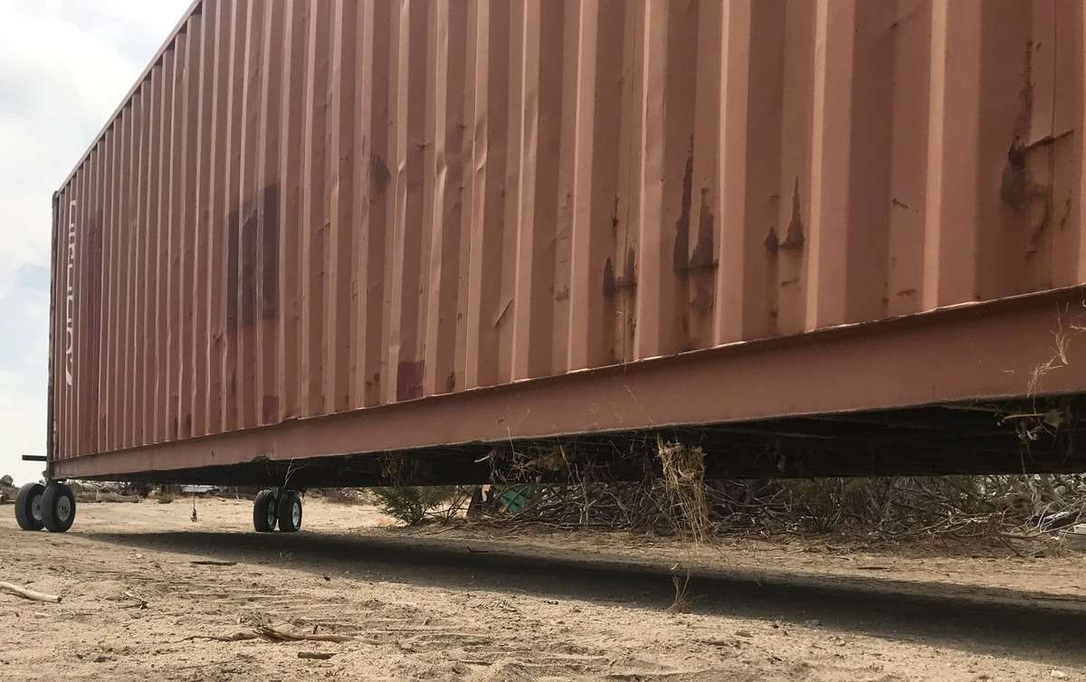Rusty shipping container on wheels in a desert area.