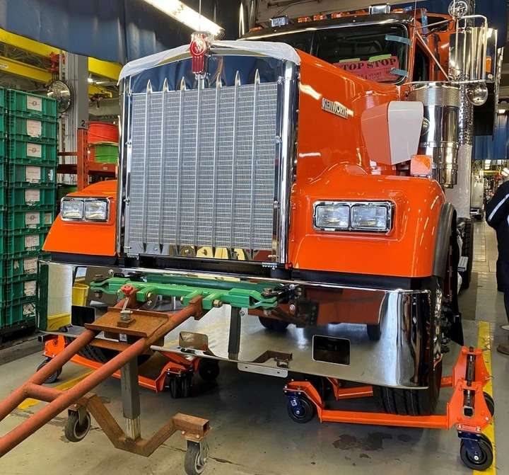 Orange Kenworth semi-truck in a workshop setting.