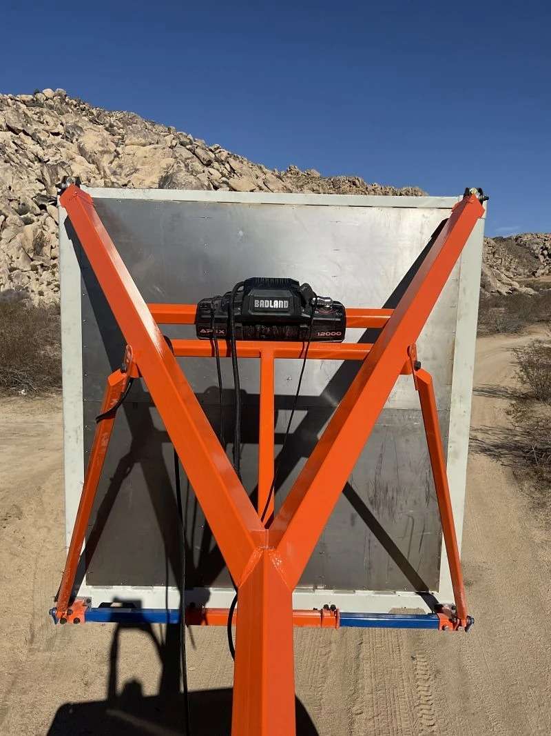 Orange hoist crane lifting gray box outdoors.