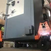 Forklift moving a large metal cabinet in warehouse.