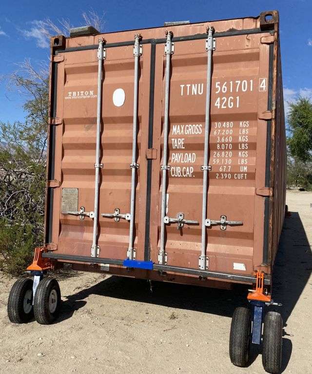 Rusty shipping container on wheeled trailer outdoors.